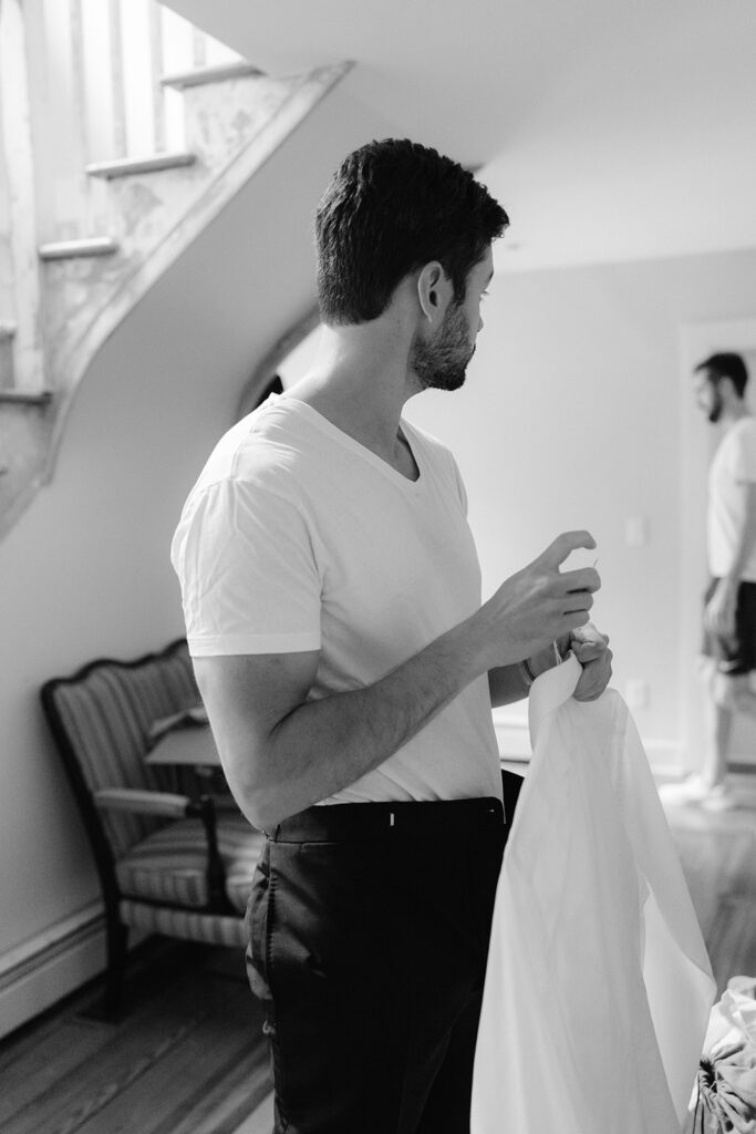 Groom getting ready photo holding his white button up shirt. 
