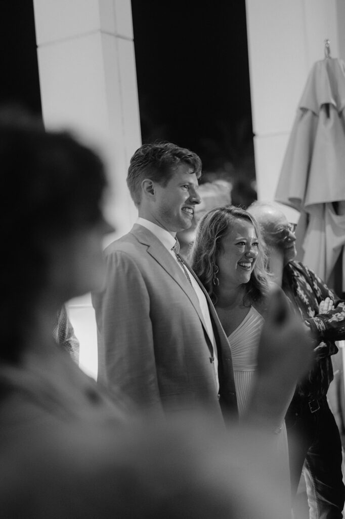 Candid moment of a couple smiling during a speech at their wedding welcome party.