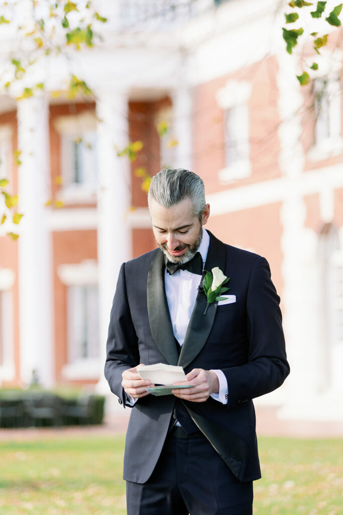 Groom reading a handwritten letter from the bride outside the Bourne Mansion.
