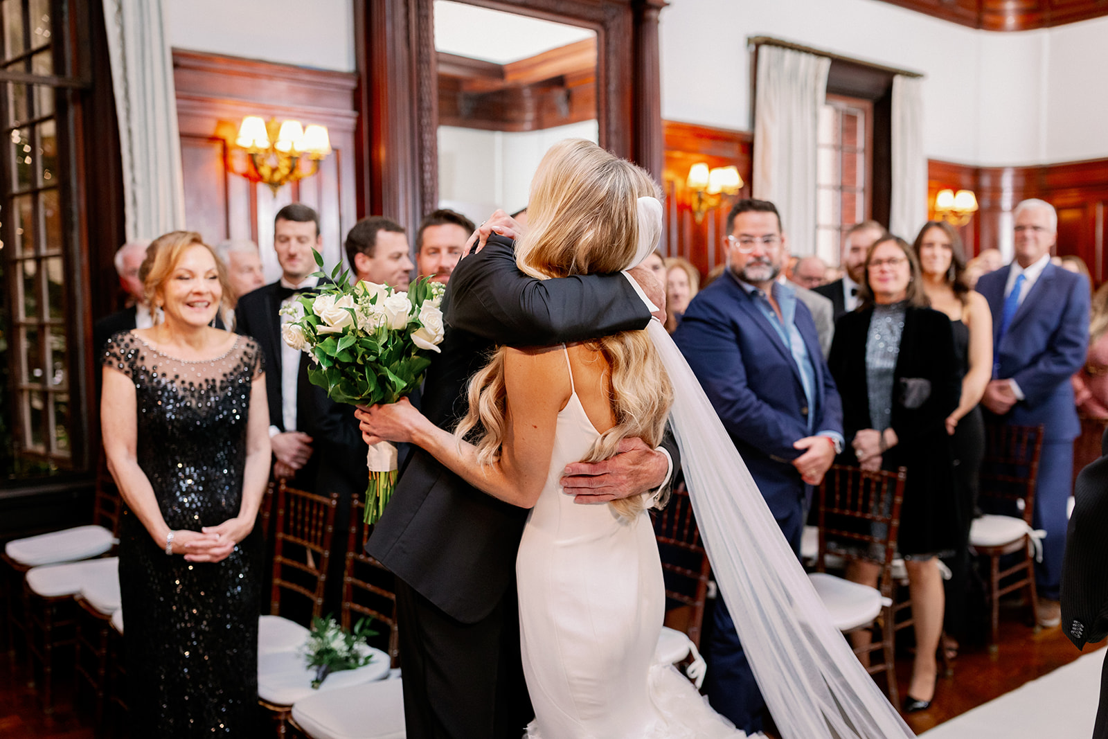 Bride hugging her dad after walking down the  aisle at her Bourne Mansion indoor wedding ceremony.
