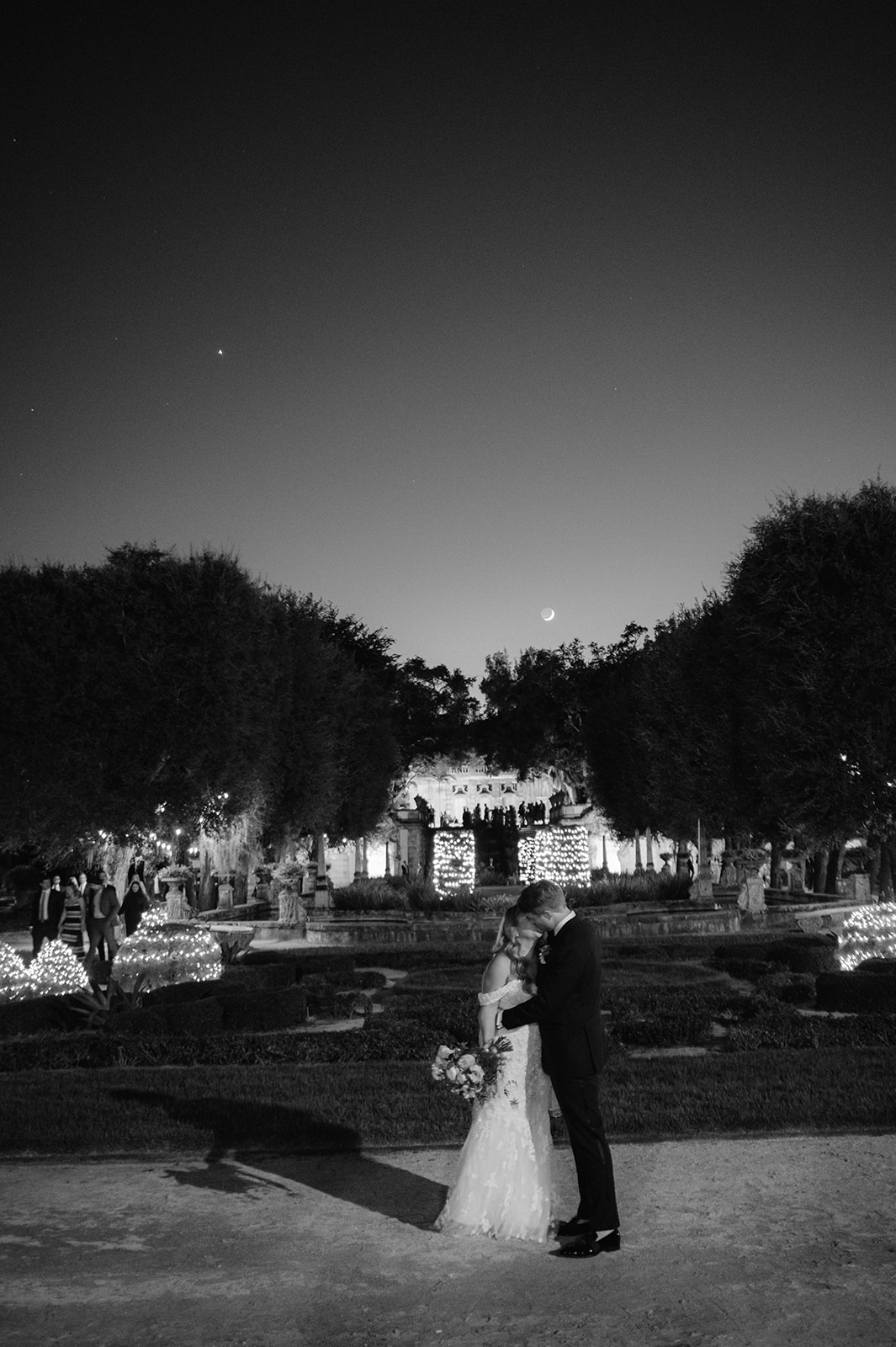 Bride and groom kissing under a crescent moon at Vizcaya Gardens. 