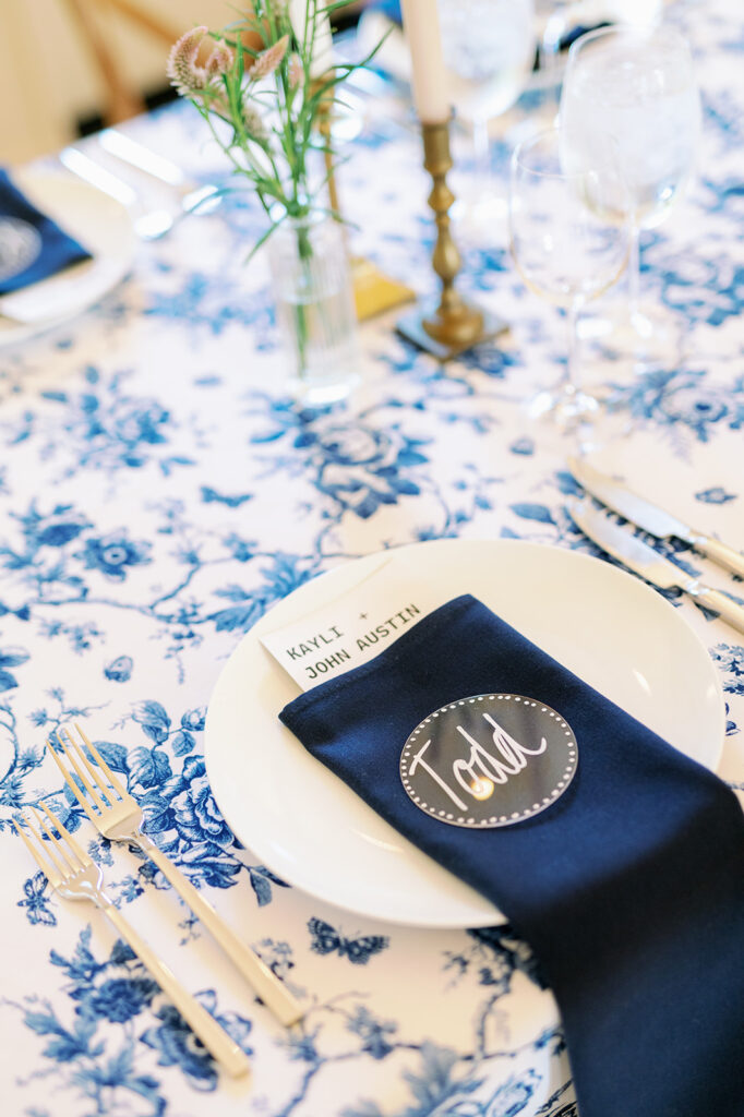 Wedding place setting with blue floral tablecloth and navy blue napkins with personalized name cards. 