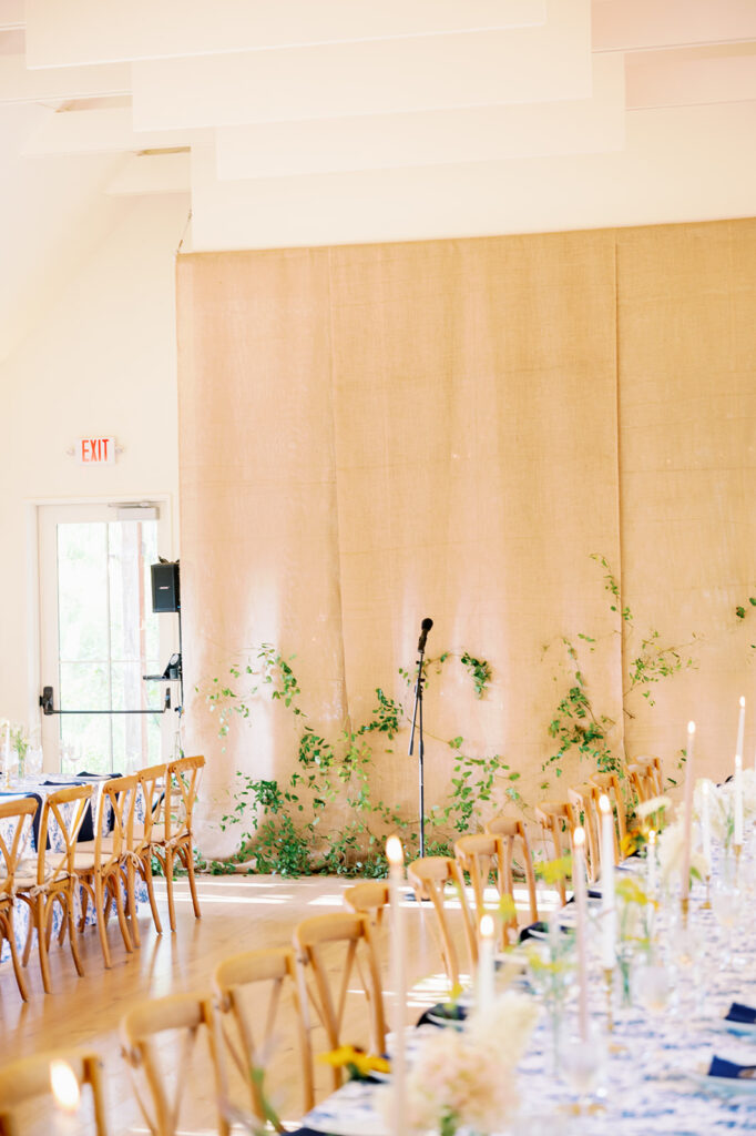 Wedding rehearsal dinner with a tan backdrop adorned with greenery for speeches. 