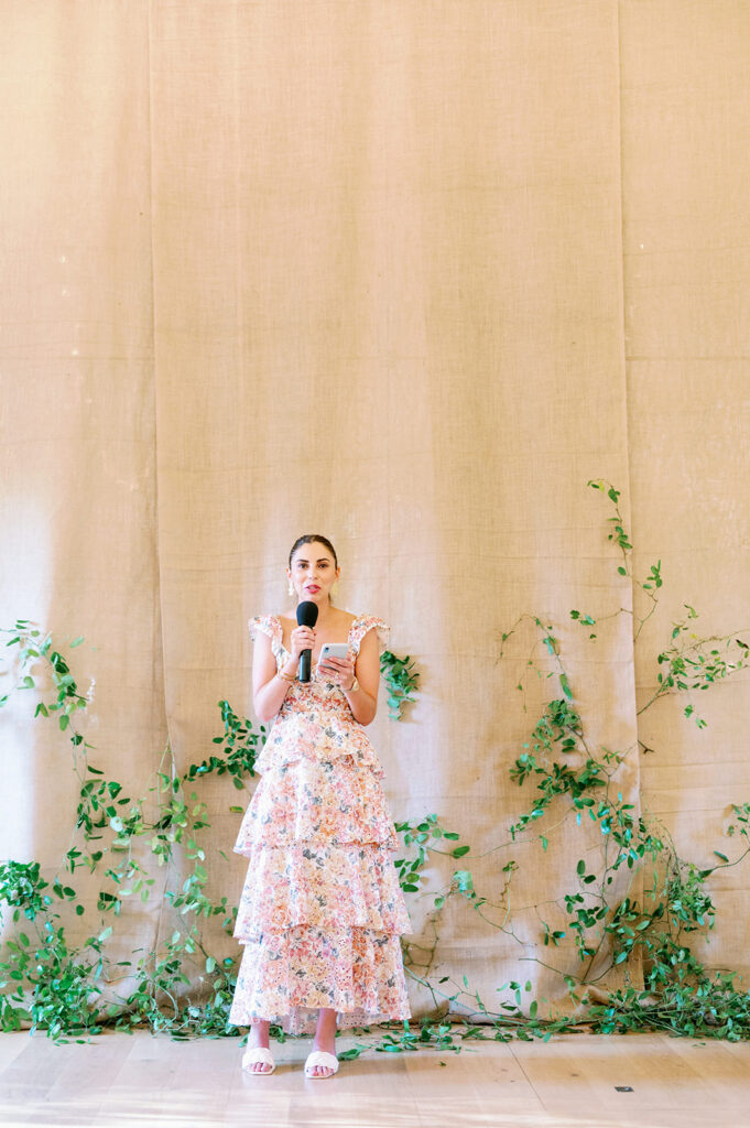Woman in a layered floral dress giving a speech at a wedding rehearsal dinner at Troutbeck Hotel.