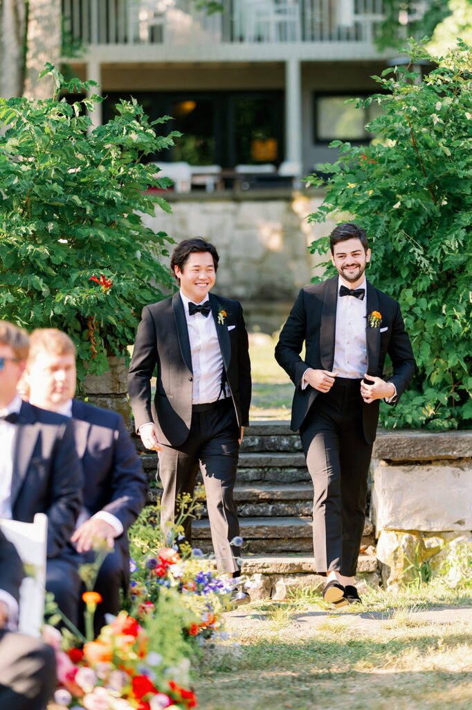 Groom and best man walking down a floral lined aisle at Troutbeck.