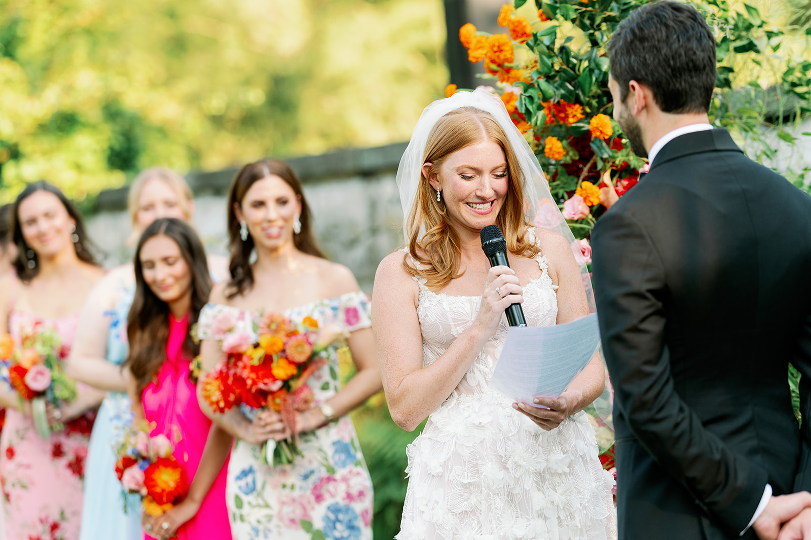 Bride saying her vows during a garden wedding ceremony with her bridesmaids in the background.