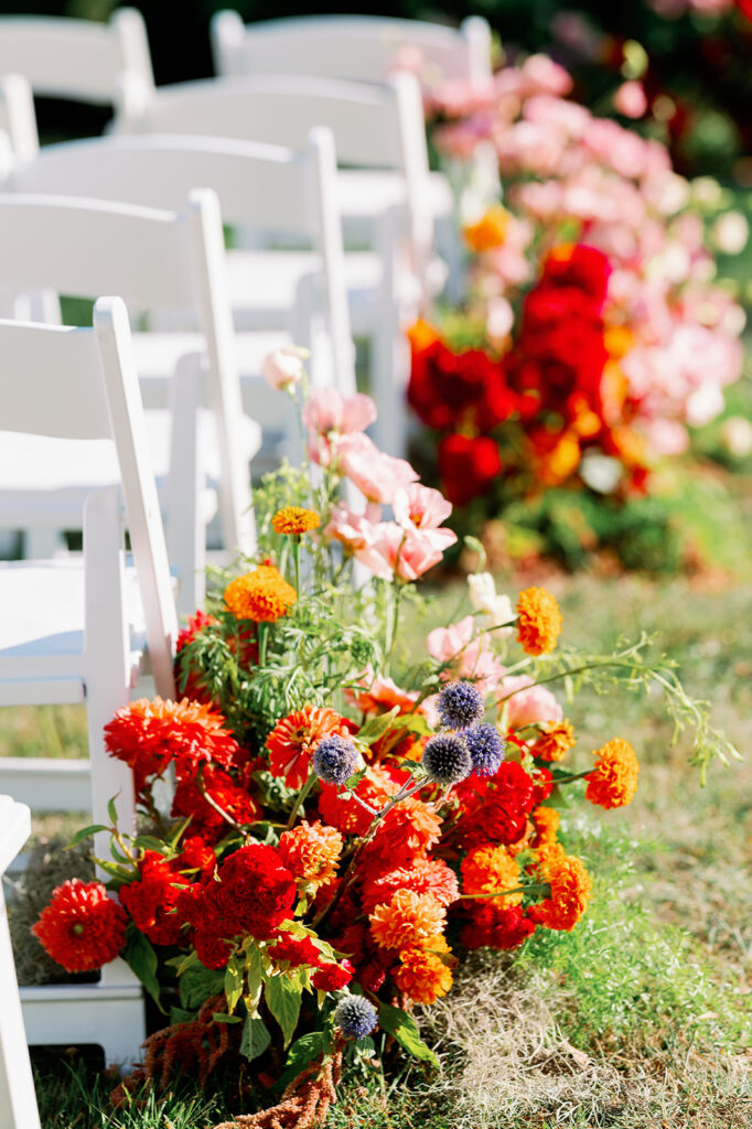 Vibrant wildflower floral arrangements lining an oudoor wedding ceremony aisle.