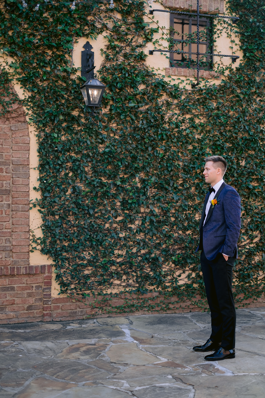Groom anxiously awaiting the first look with his bride against a climbing ivy wall outside Bella Collina.