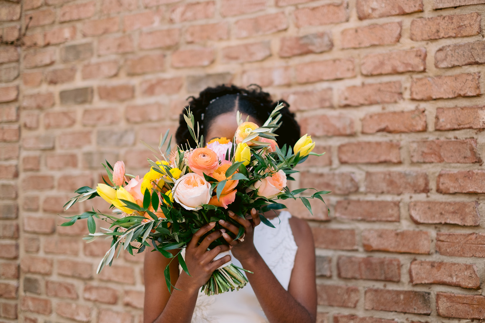 Bride holding her colorful sunset-inspired bouquet in front of her face.