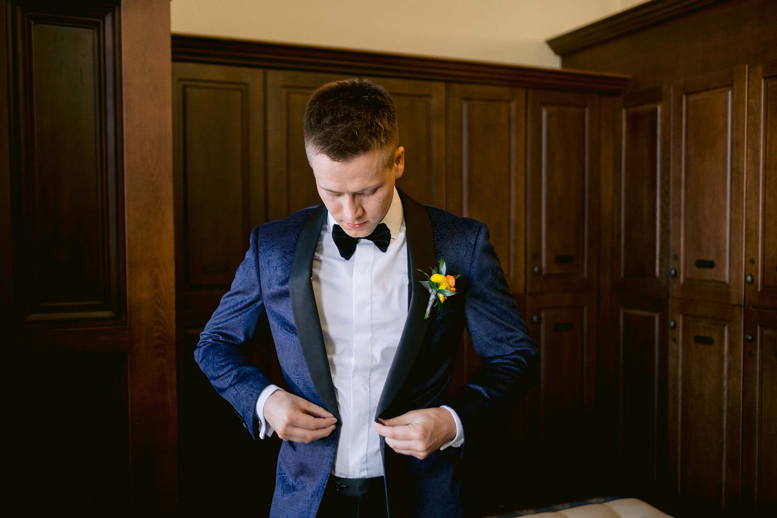 Groom buttoning his blue velvet tuxedo with paisley detailing from Robbie & Co.