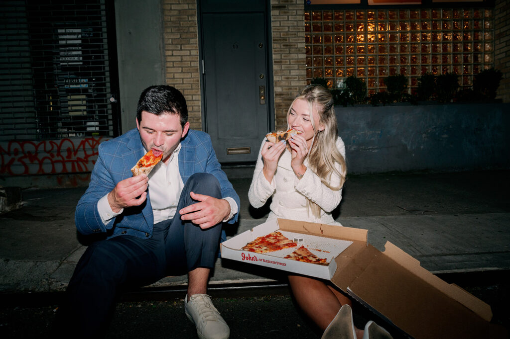 Couple eating pizza on a New York City curb during their city engagement photos.
