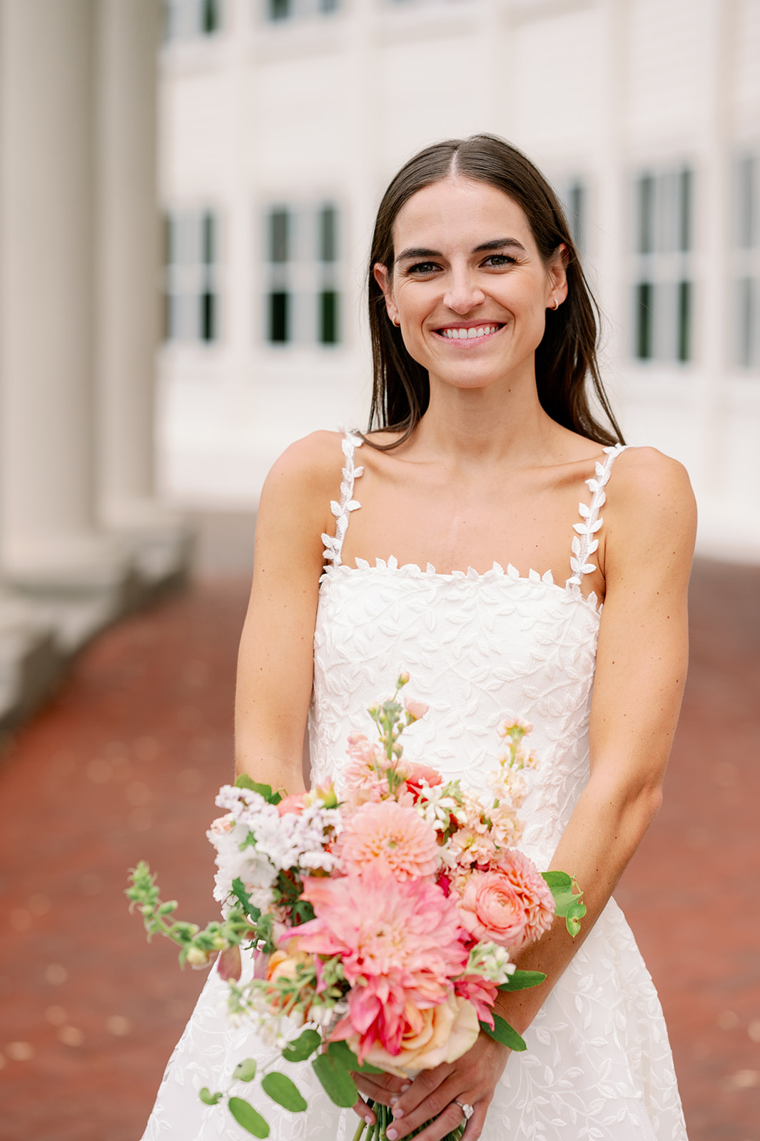 Waist up bridal portrait of Carly outside the Minikahda Club holding a pink floral bouquet.