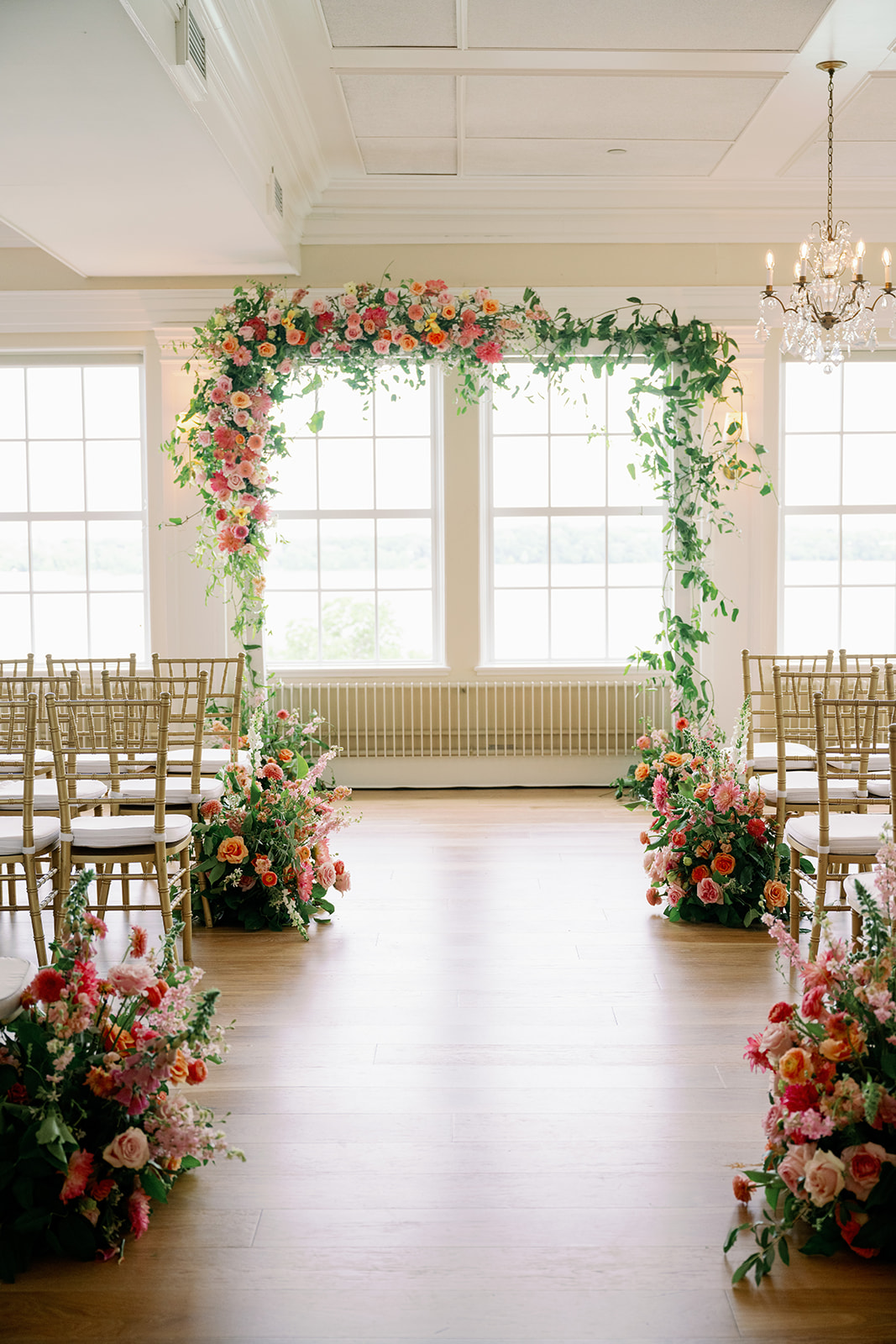 Indoor wedding ceremony at Minikahda Club with a floral arch and large floral arrangements lining the aisle.