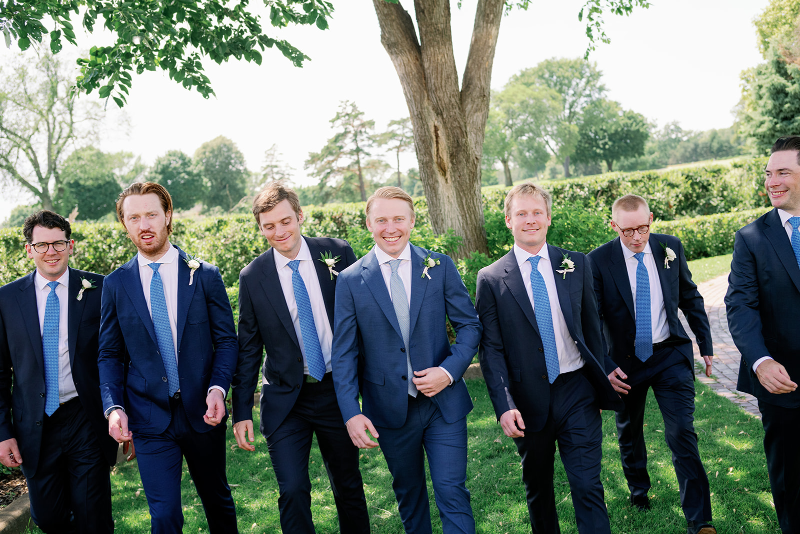 Todd and six groomsmen in navy blue suits and ties walking toward the camera.
