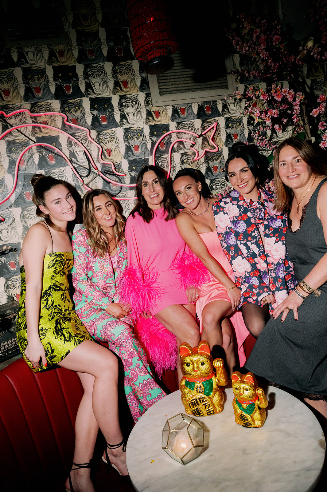 Bride Caroline and bridal shower guests wearing vibrant attire posing in a booth at Peachy's bar. 