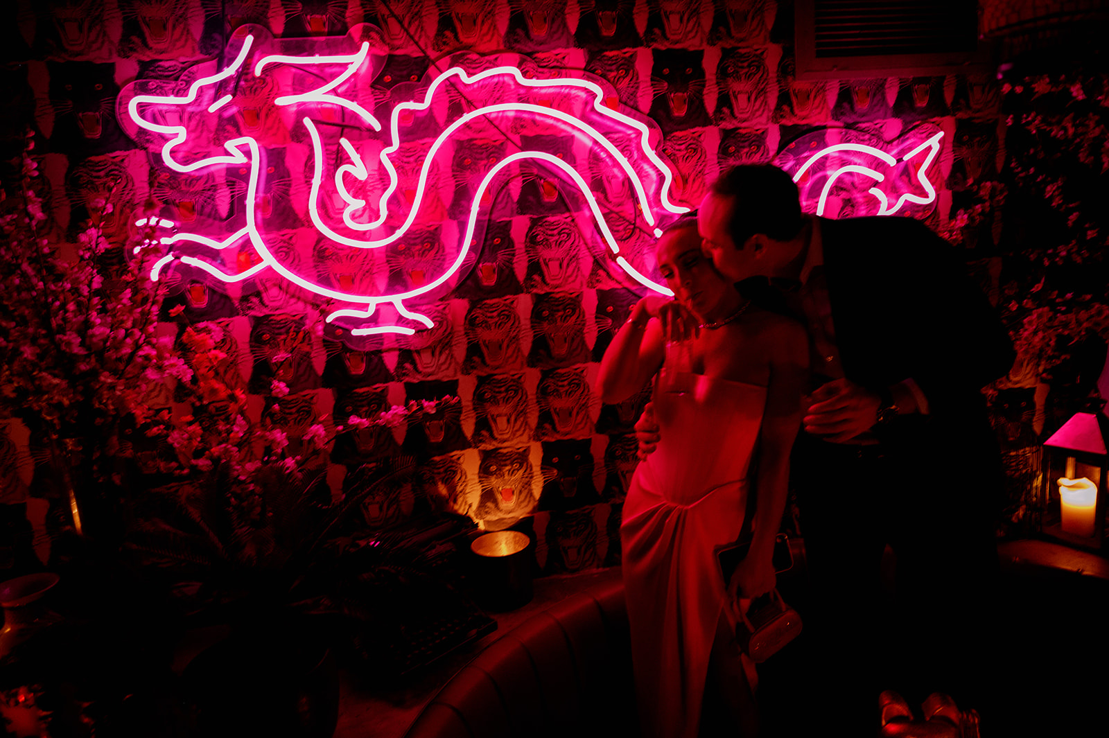 Groom kissing the bride's cheek under Peachy's neon dragon in Chinatown, New York.