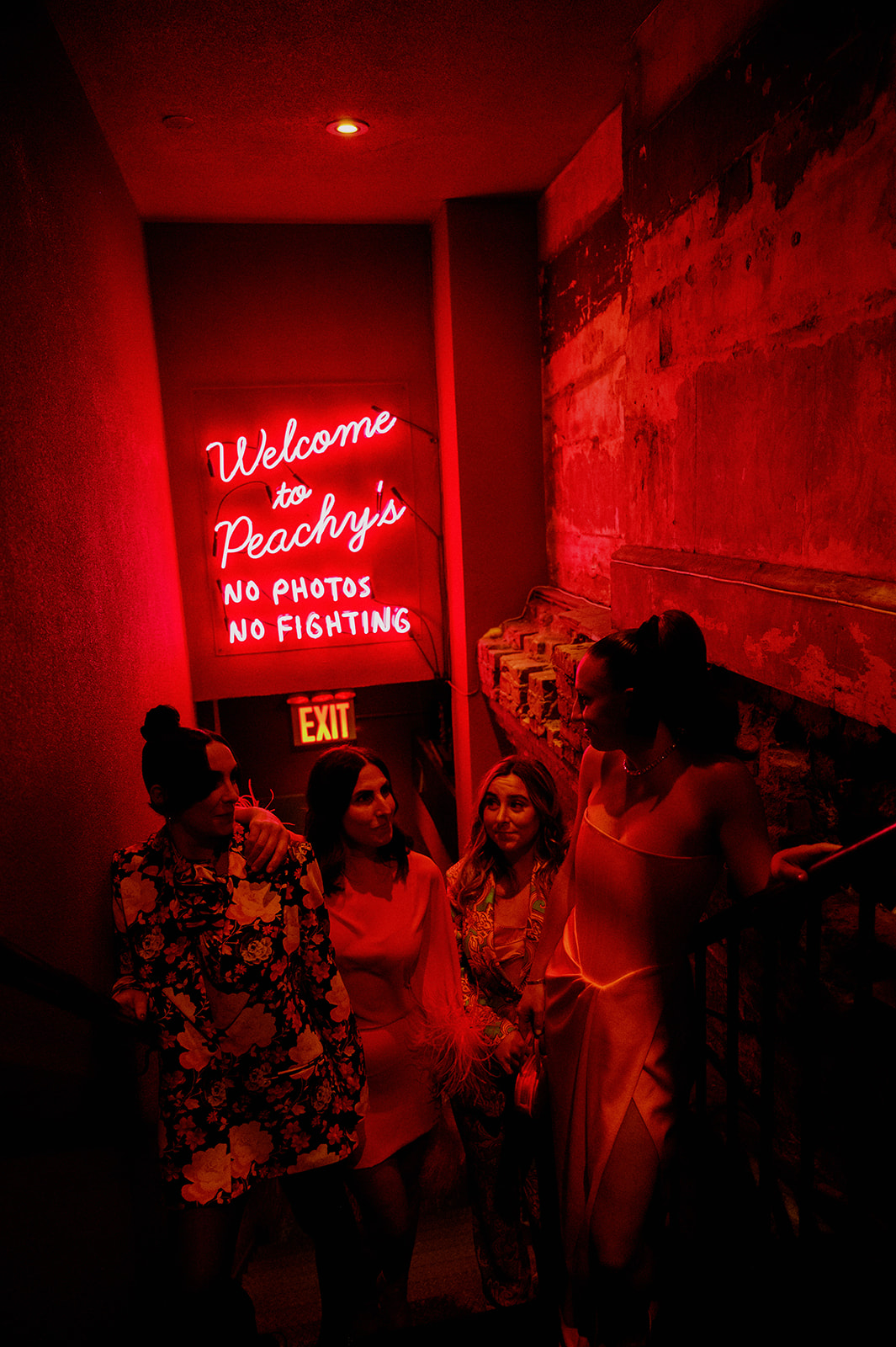 Bride Caroline and sisters posing under the red neon glow of the Welcome to Peachy's sign in Chinatown for her bridal shower.