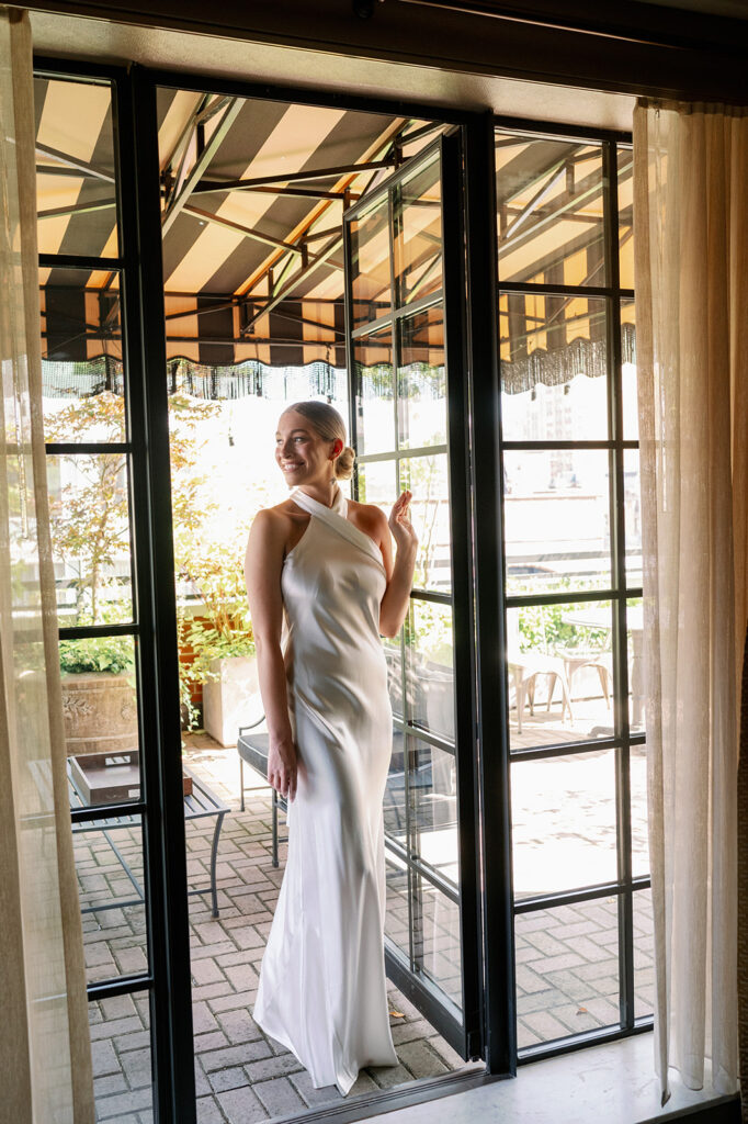 Bride stands in a door frame, bathed in natural light at the Soho Grand Hotel. 