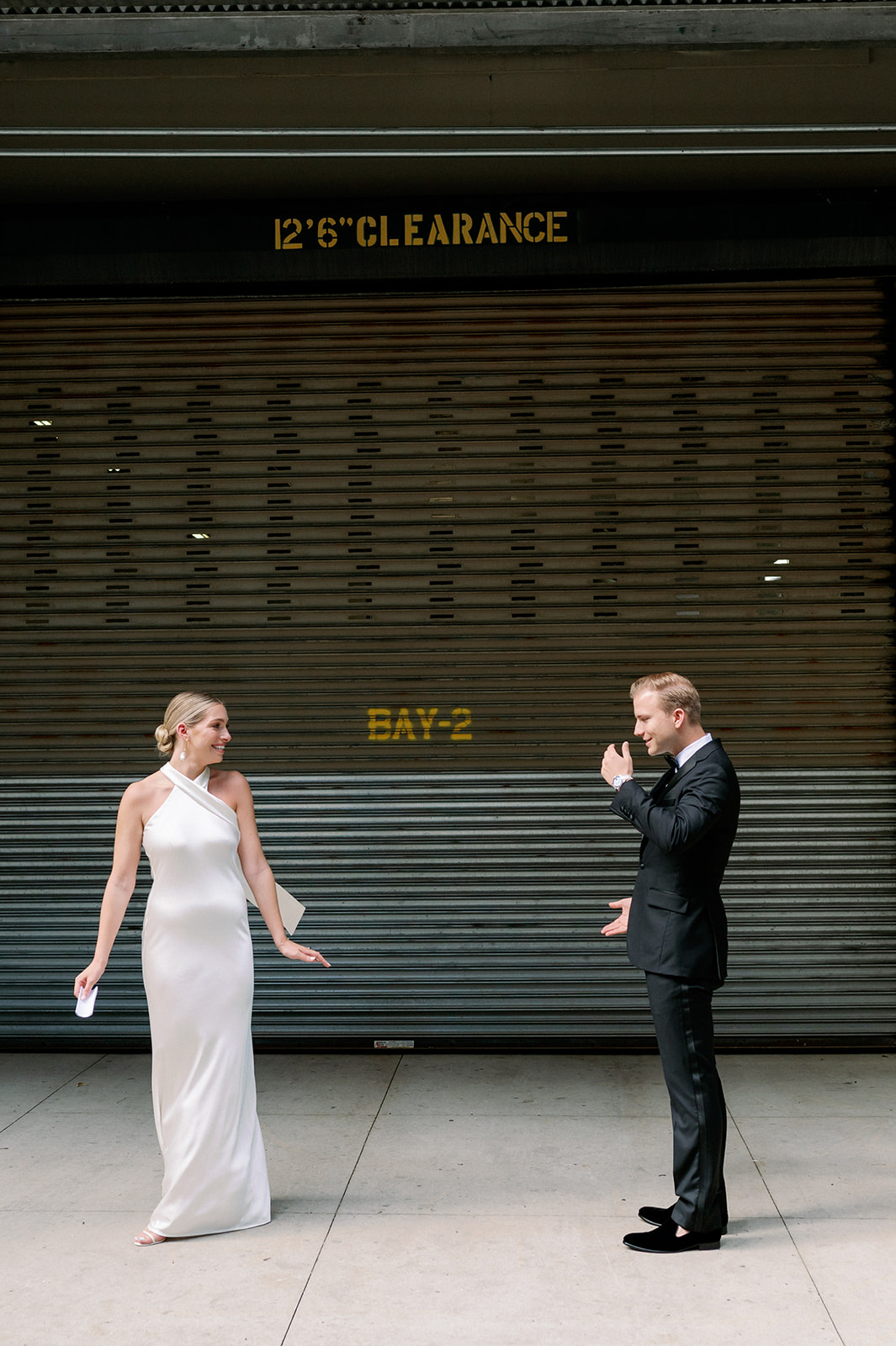 Groom captivated, watching bride twirl, taking in her beauty in front of a black garage. 
