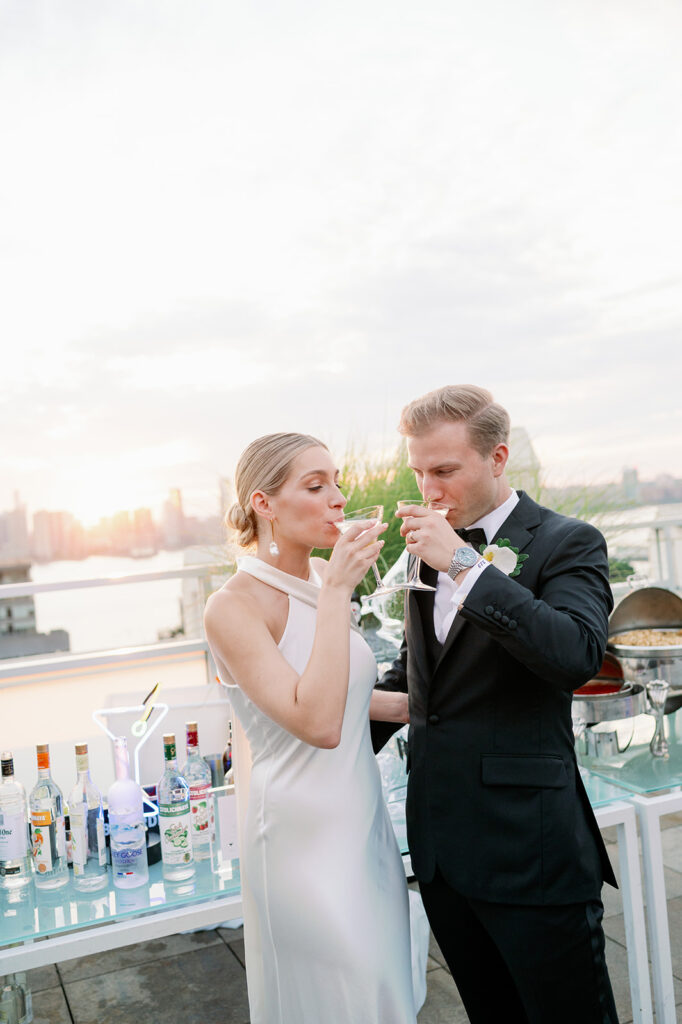 Tribeca Rooftop wedding cocktail hour. The bride and groom share a drink, skyline and sunset painting a romantic backdrop.