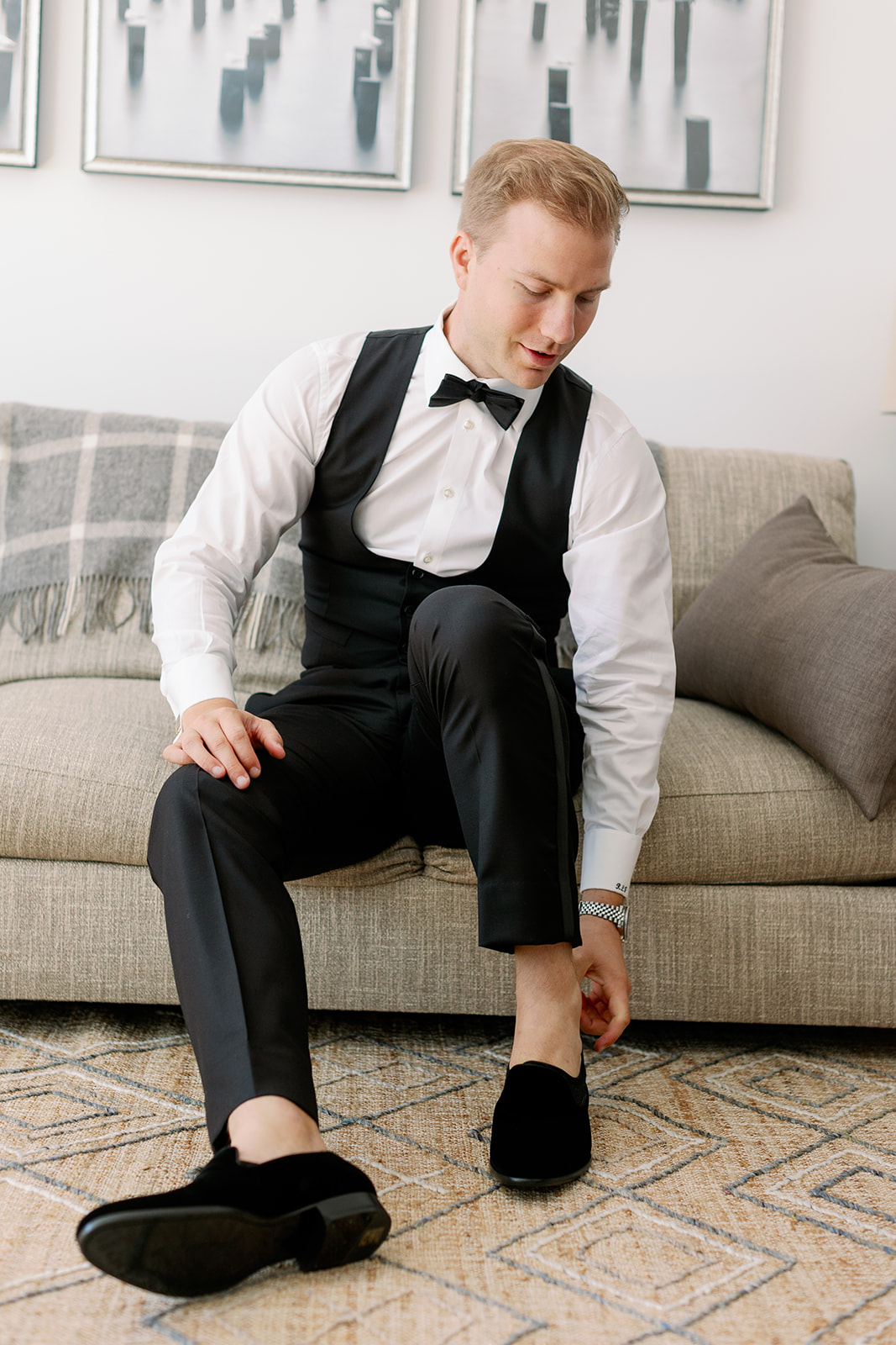 Groom readies for the big day, a candid portrait as he sits on a couch, putting on his shoes.