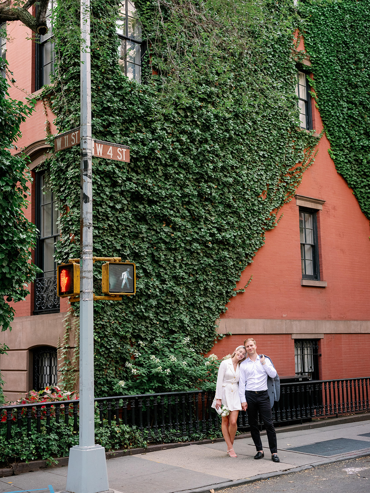 Bride and groom share a moment in Greenwich Village, framed by a brownstone adorned with greenery—a romantic New York portrait.