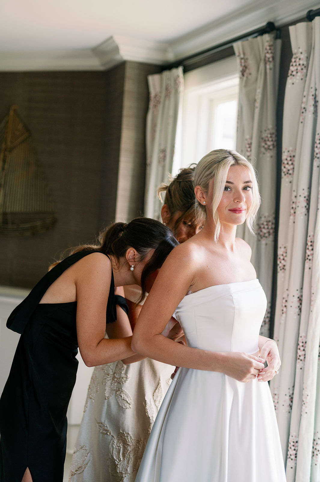 Bride getting her wedding dress zipped up by her mom and sister in the Carousel Suite at Ocean House. 