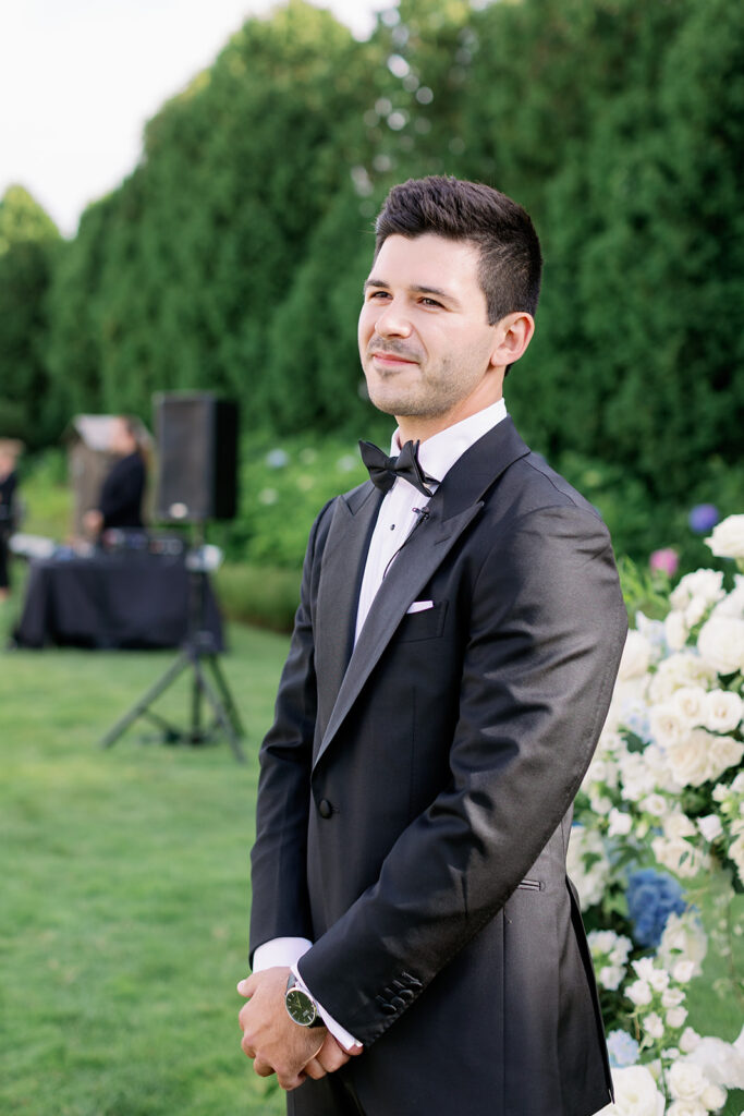 Groom smiling as he watches his bride walking down the aisle on the South Lawn at Ocean House. 