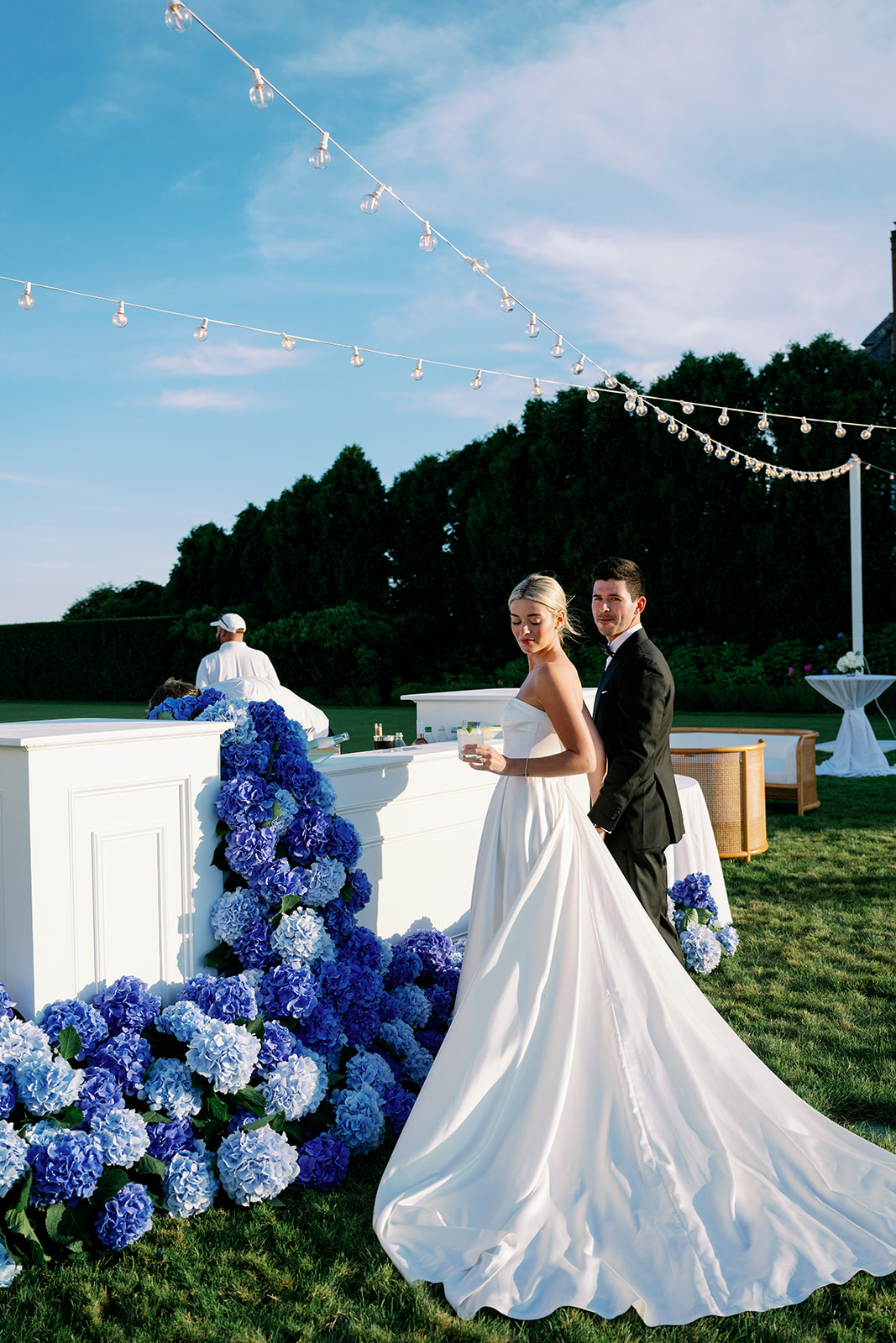 Bride and groom standing at their cocktail hour bar with cascading blue hydrangeas. 