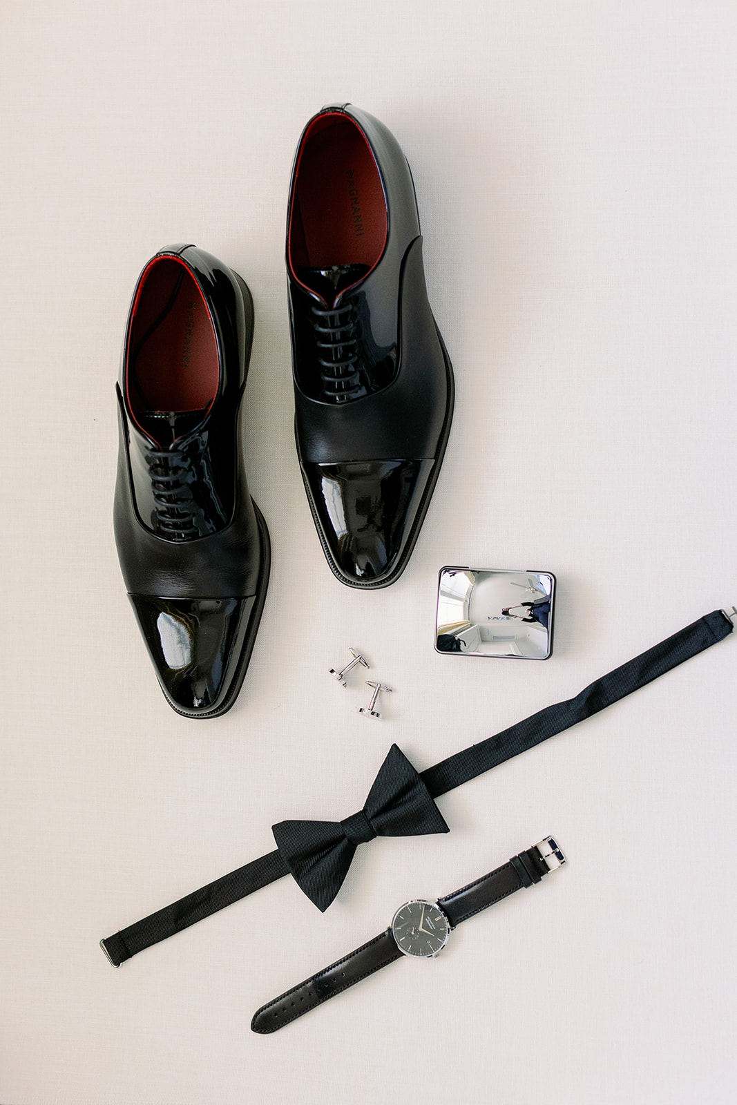 Groom wedding detail flat lay with Manolo Blahnik shoes, cufflinks, cologne, a black bowtie and watch. 