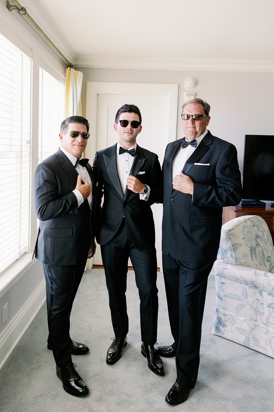 Groom and his dad and father-in-law posing and wearing sunglasses in a Ocean House hotel room. 