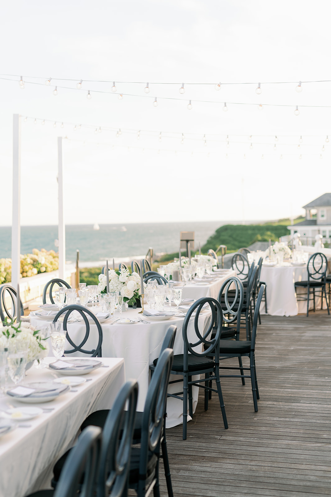 Ocean House wedding outdoor waterfront dinner with white tables and black chairs. 