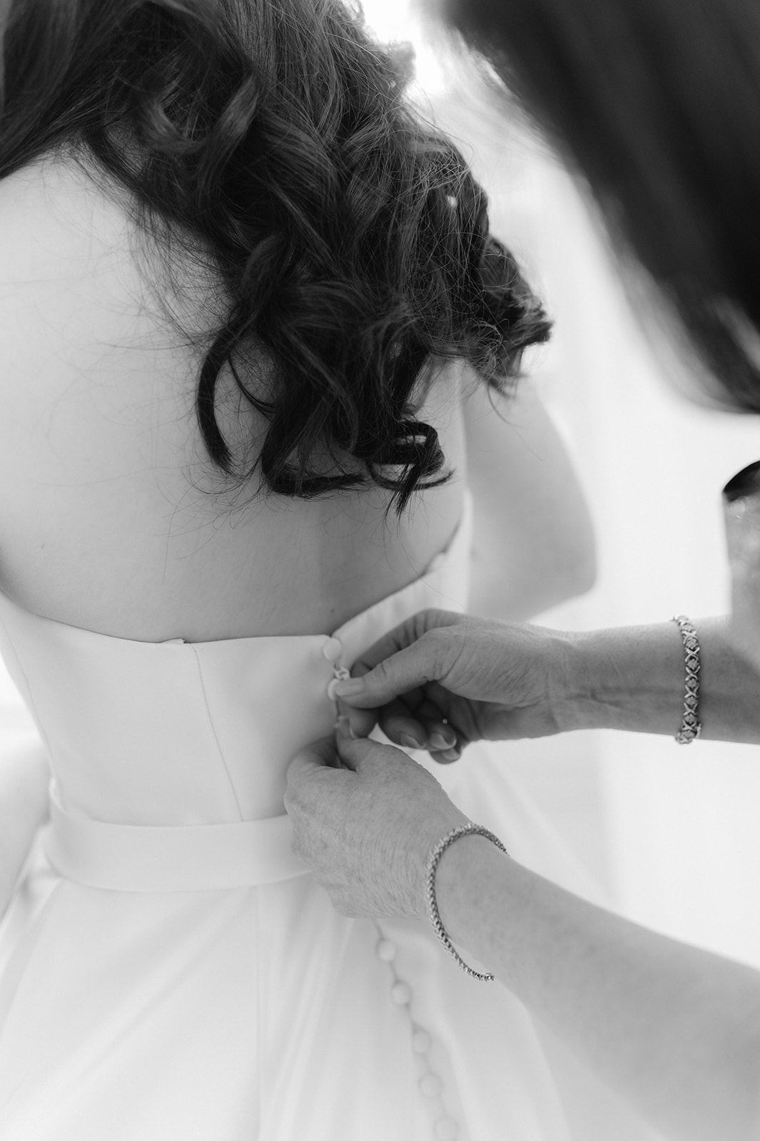 Up close black and white shot of a bride getting her wedding dress buttoned. 