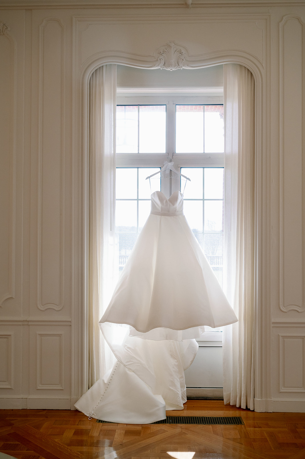 Wedding dress hanging in a well lit window at Pine Hollow Country Club. 
