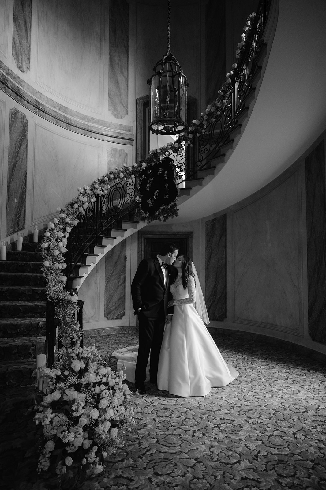 Bride and groom kissing next to a floral-lined spiral staircase at Pine Hollow Country Club.
