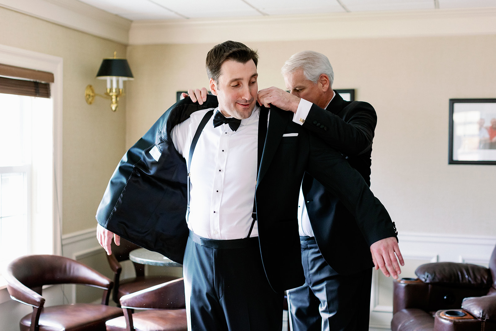 Groom's father helping groom put on his suit jacket. 