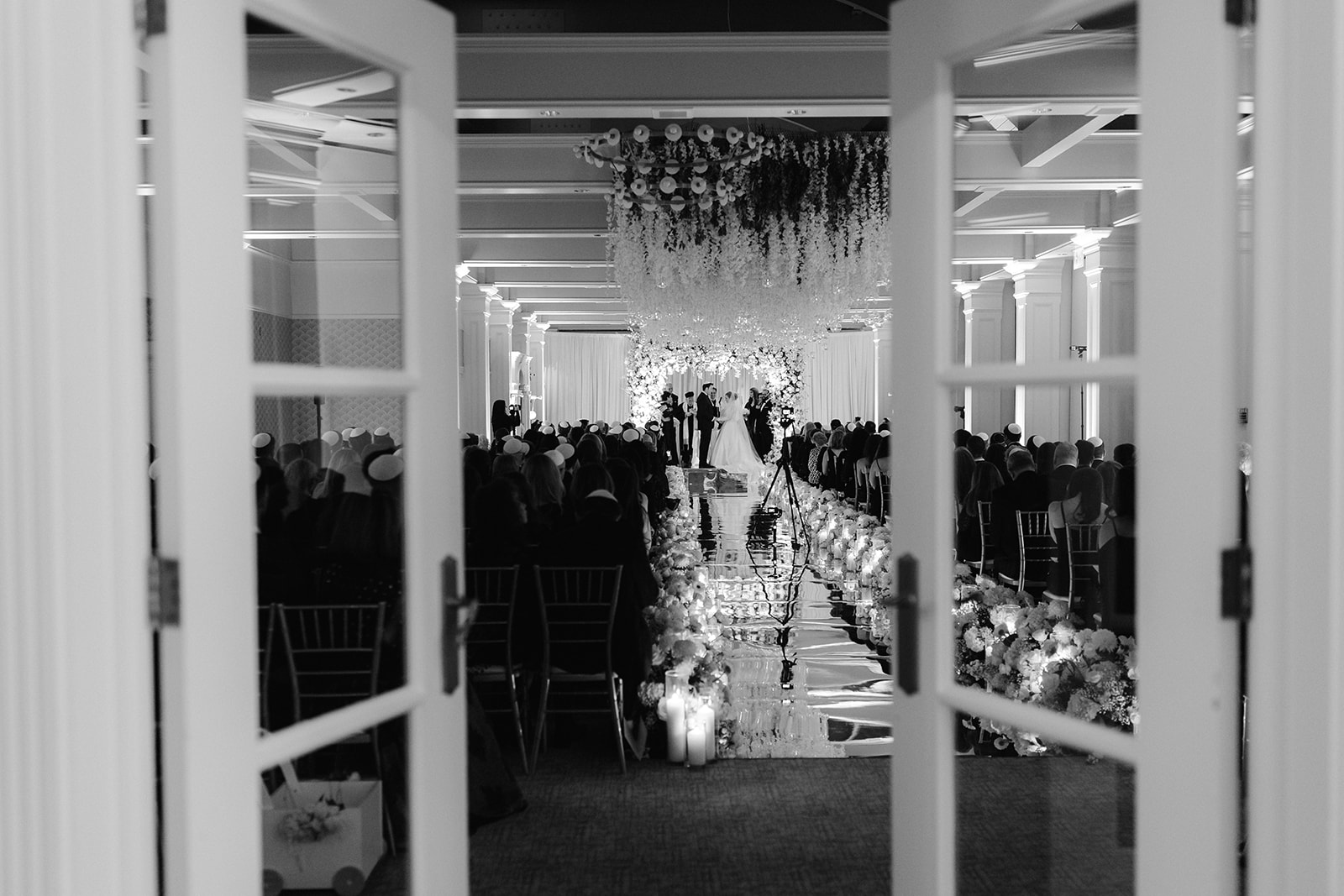 Wide angle view behind semi-closed doors of an indoor wedding ceremony at Pine Hollow Country Club.