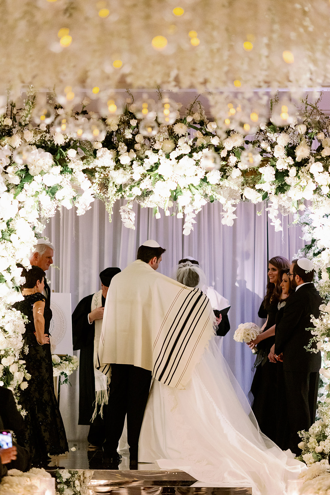Bride and groom wrapping a prayer shawl around their shoulders during their traditional Jewish ceremony.