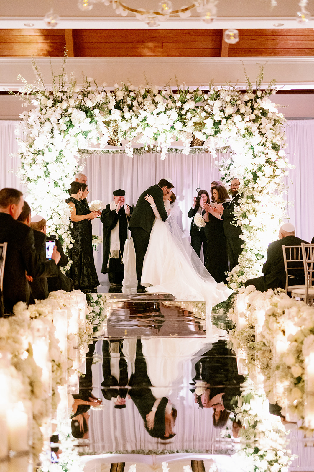 Bride and groom kissing under a large floral chuppah at Pine Hollow Country Club.