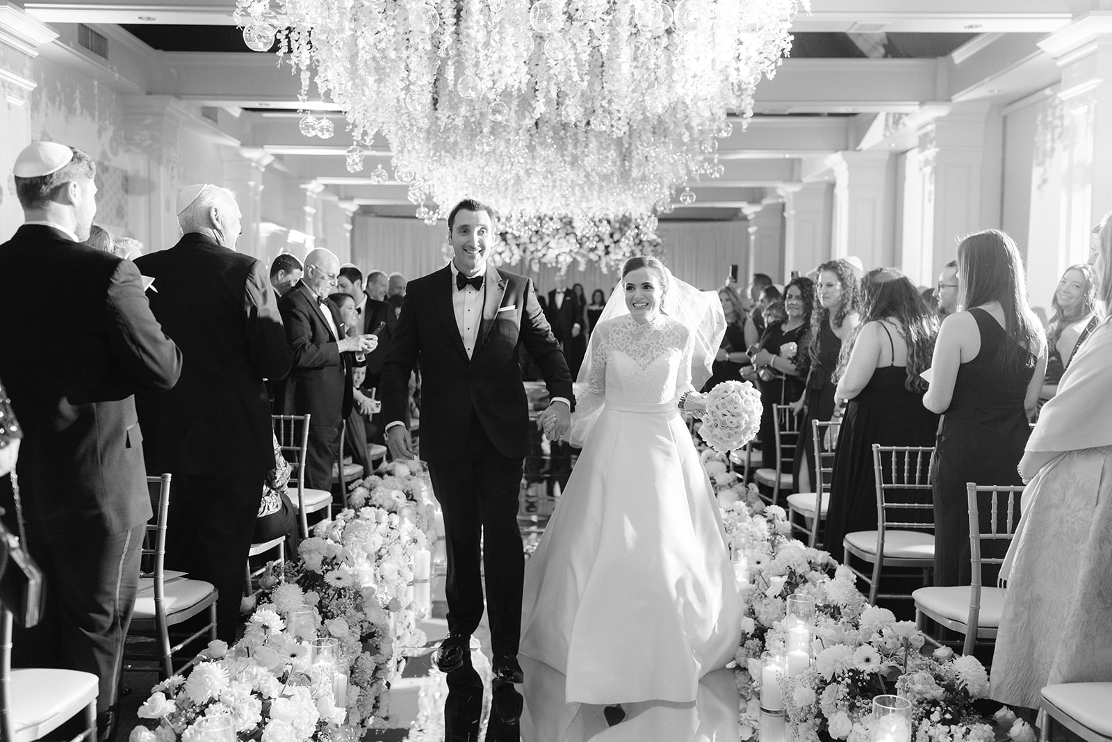 Bride and groom recessional with a reflective aisle and hanging florals. 