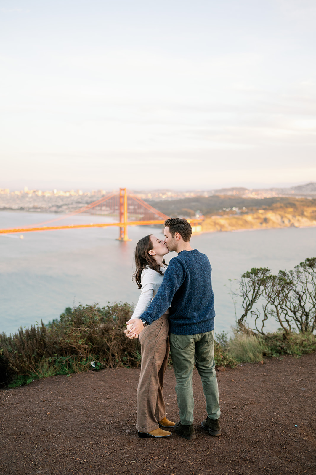 Couple kissing in front of the Golden Gate Bridge at Marin Headlands. 