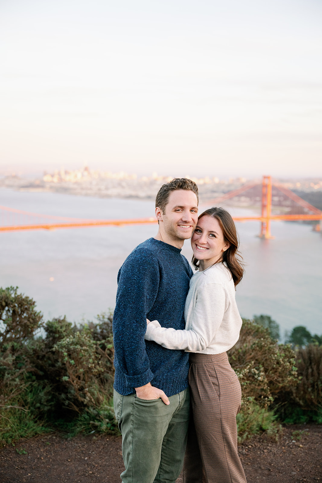 Couple posing with the Golden Gate Bridge in the background at Marin Headlands. 