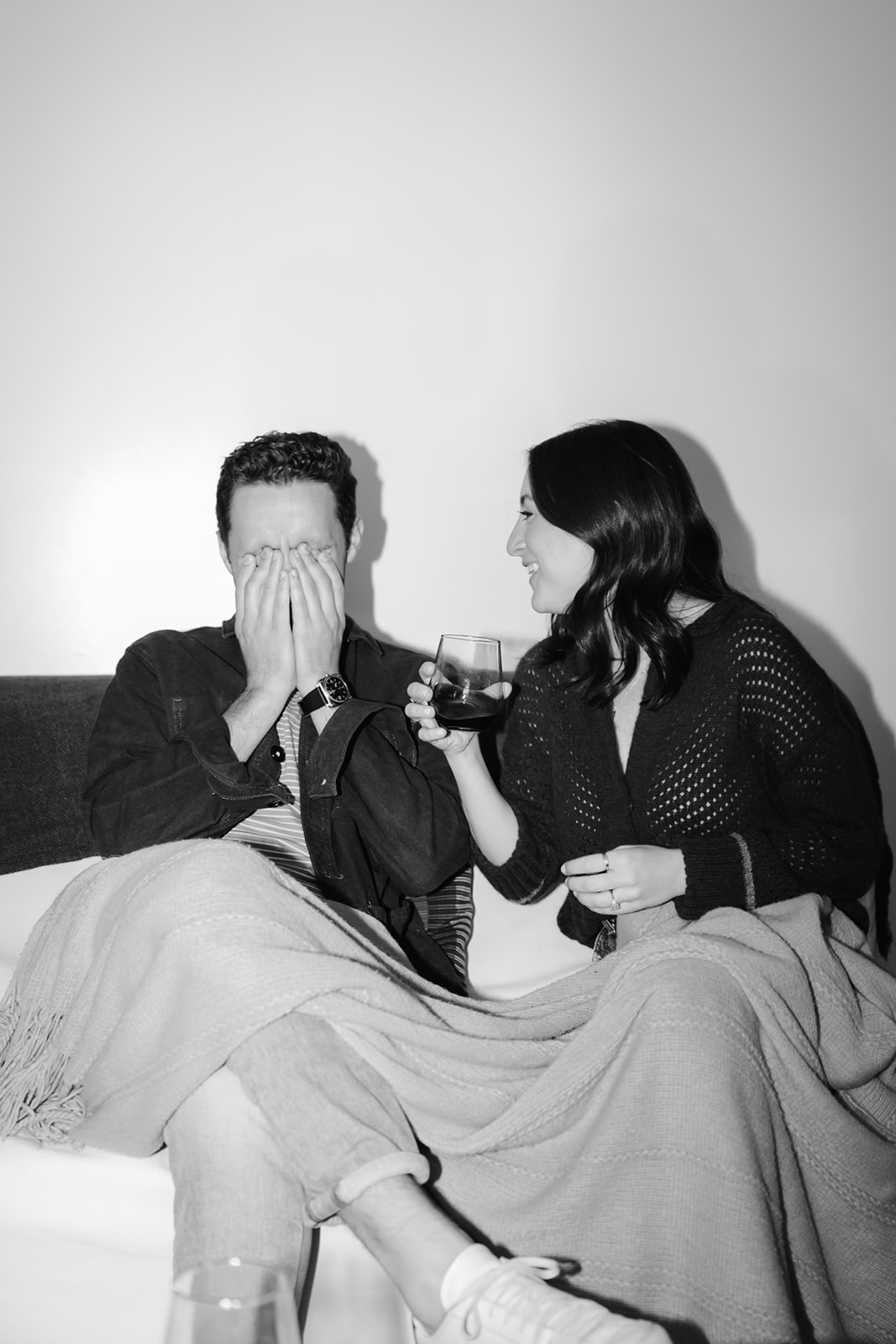 Candid couple drinking a glass of wine cozied up on their couch at home.
