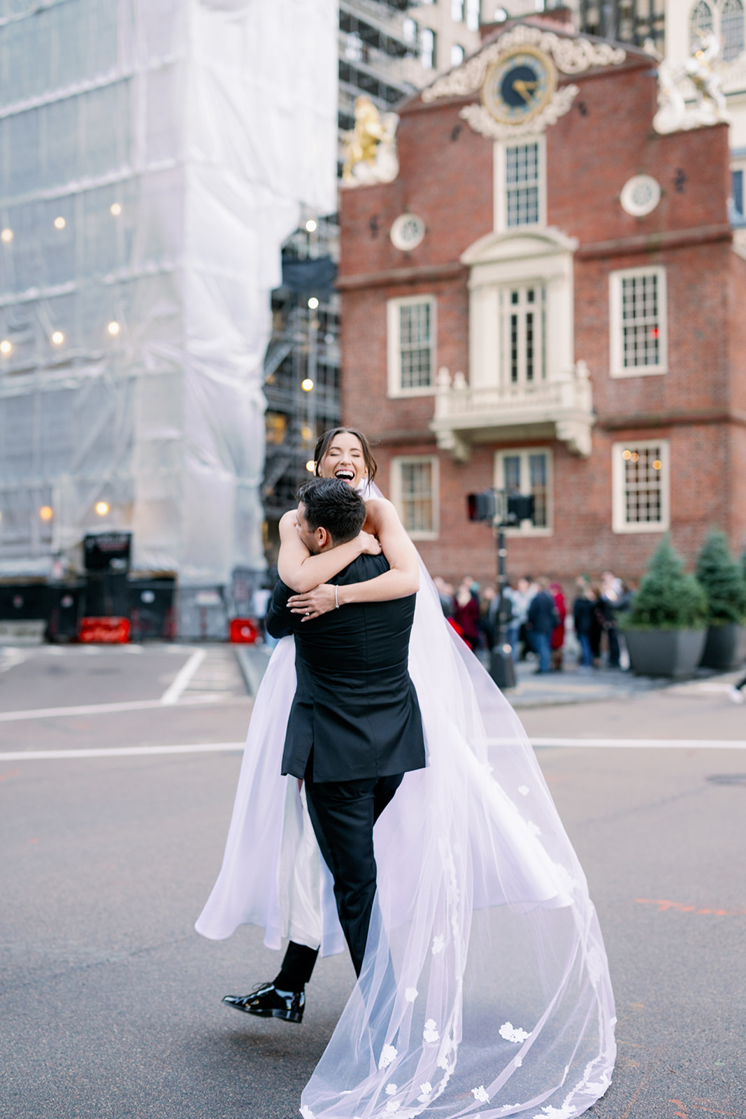 Groom picking up his bride to cross the street outside the Boston State House. 