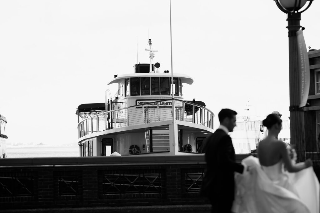 Bride and groom walking in front of a ferry boat at Rowes Wharf in Boston. 