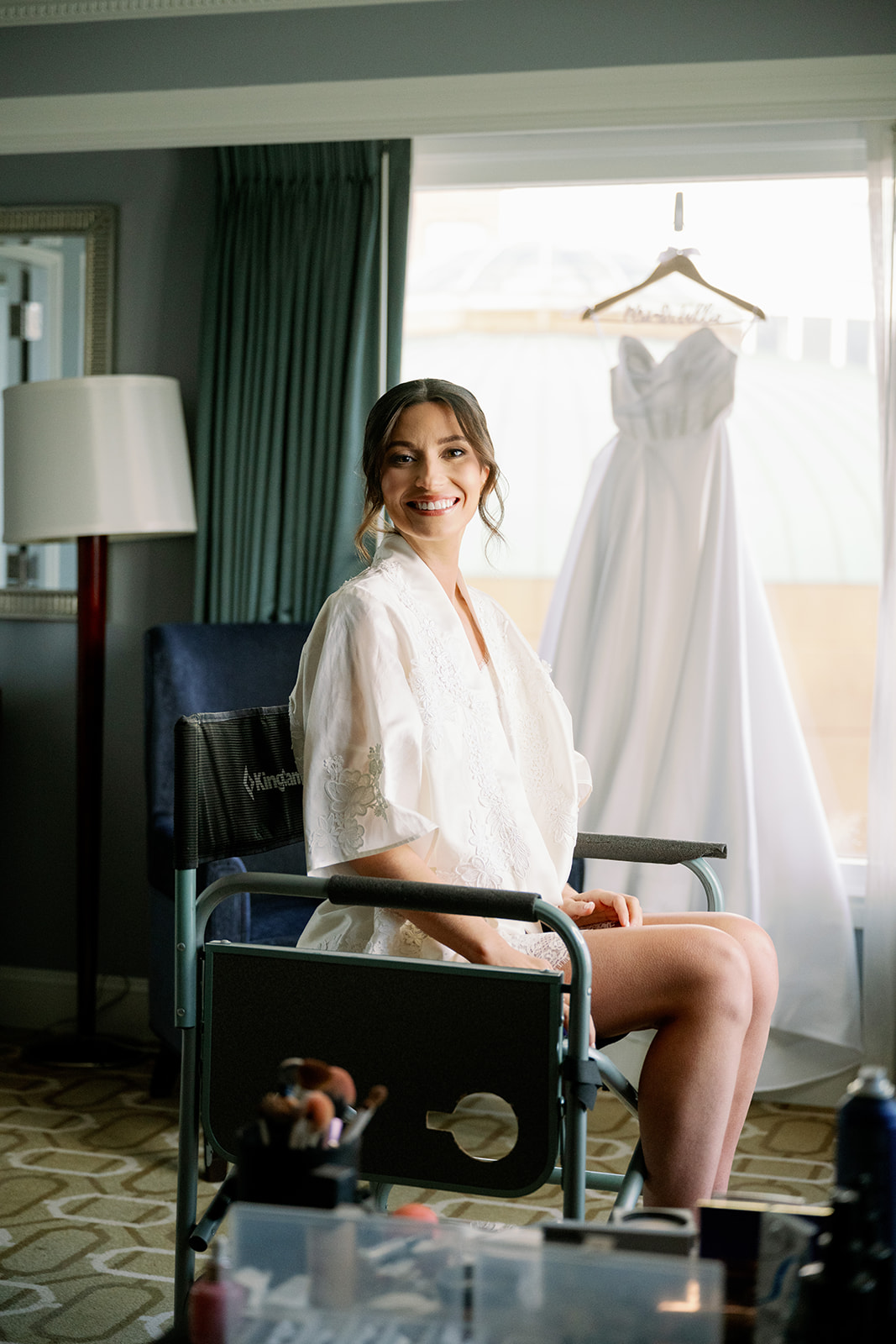 Bride in a custom white getting ready robe smiling after getting her hair and makeup done.