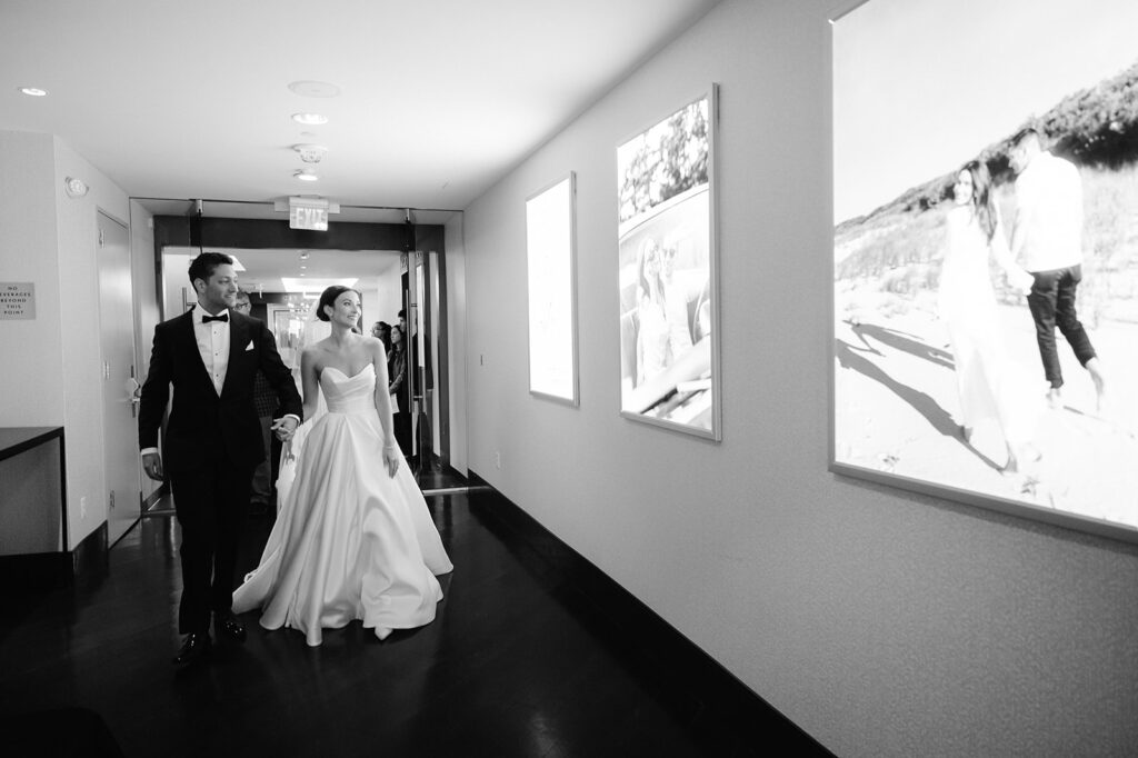 Bride and groom walking down the hallway at The State Room in Boston with illuminated posters on the wall. 