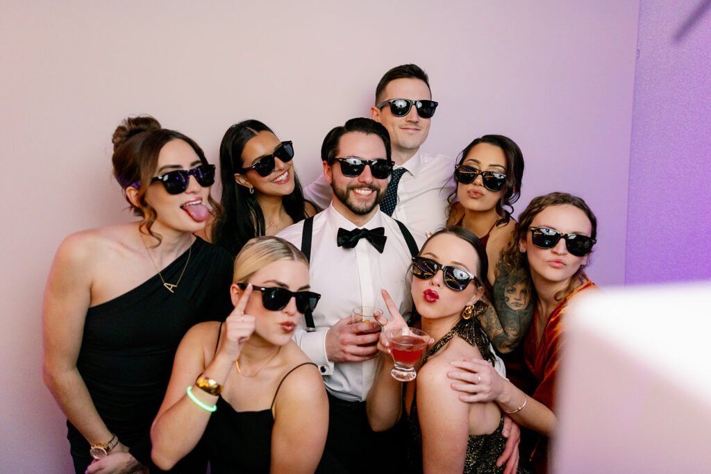 Wedding guests taking a photo in the photo booth with sunglasses and drinks. 